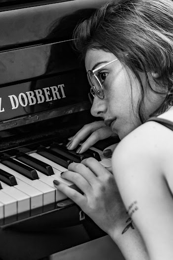 Woman Wearing Eyeglasses leaning on Piano