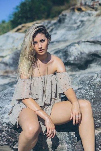 woman wearing gray and black polka-dotted cold-shoulder rompers while sitting on stone