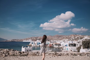 Woman Wearing Gray Shirt Standing in Front White Houses Beside Body of Water