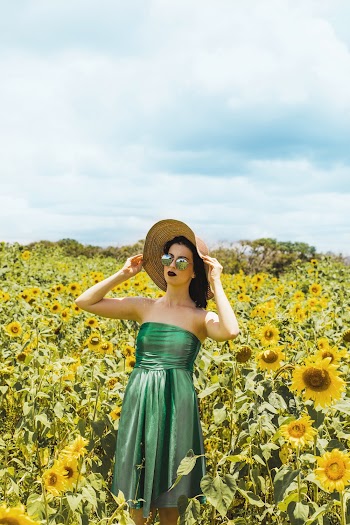 Woman Wearing Green Tube Dress And Sunhat Standing In The Middle Of Sunflower Meadow