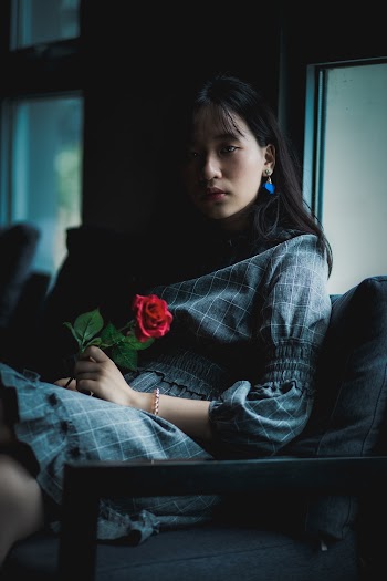 Woman Wearing Grey Dress Sitting on Sofa Holding Red Rose