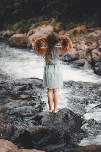 Woman Wearing Grey Dress Standing on Rock Beside Flowing Body of Water