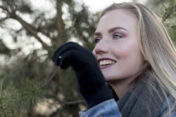 Woman Wearing Grey Scarf Holding a Pine Leaf While Smiling