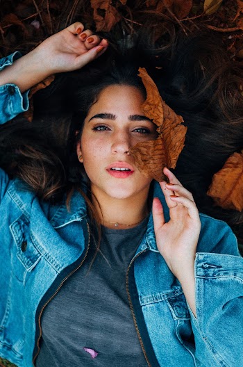 Woman Wearing Grey Shirt and Blue Denim Jacket Lying on Grass With Withered Leaves
