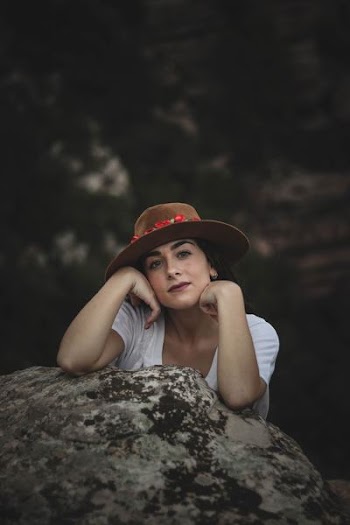 woman wearing hat leaning on gray rock formation