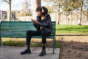 woman wearing headphones and touching phone sitting on park bench on a fall day