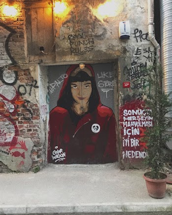 Woman Wearing Hooded Jacket Painting on Closed Door Showing Lighted Outdoor Lamp