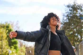 woman wearing jacket dancing in park on a fall day with arms open looking up