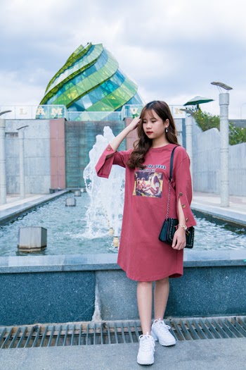 Woman Wearing Maroon Crew-neck Long-sleeved Dress Standing Next to Fountain Under Cloudy Sky