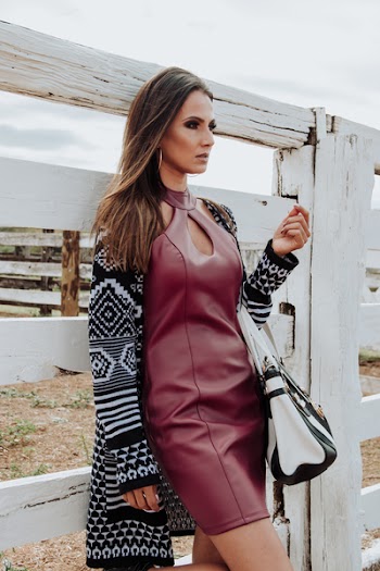 Woman Wearing Maroon Leather Dress and Cardigan Leaning on White Plank Wall