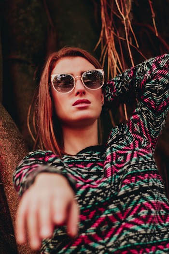 Woman Wearing Multicolored Tribal Sweater and Sunglasses Standing and About to Raise Her Right Hand