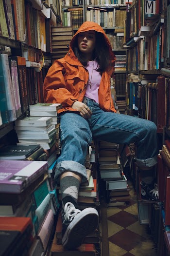 Woman Wearing Orange Jacket Sitting Inside Library