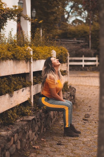 Woman Wearing Orange Off-shoulder Shirt and Gray Pants Sitting on Ledge