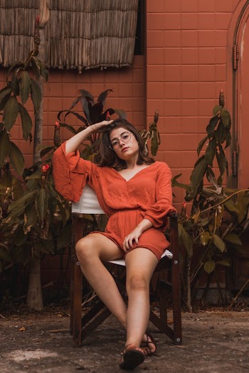 Woman Wearing Orange Plunging Neck Long-sleeve Rompers Sitting on Chair