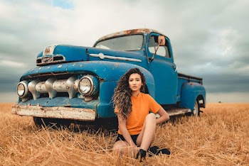 Woman Wearing Orange Shirt Sitting Next to Blue Classic Pickup Truck