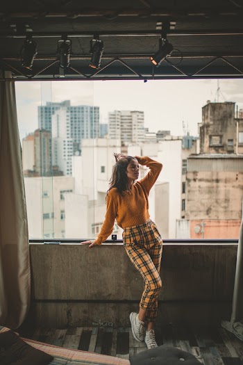 Woman Wearing Orange Sweater and Orange and Black Plaid Pants Standing Under Track Lights