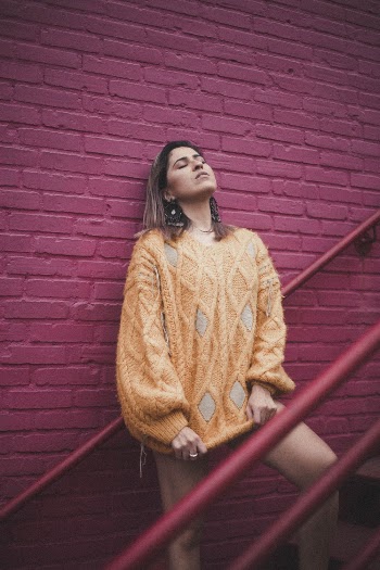 Woman Wearing Orange Sweater Leaning on the Wall