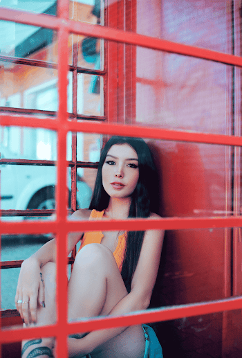 Woman Wearing Orange Tank Top Sitting Near the Red Fence