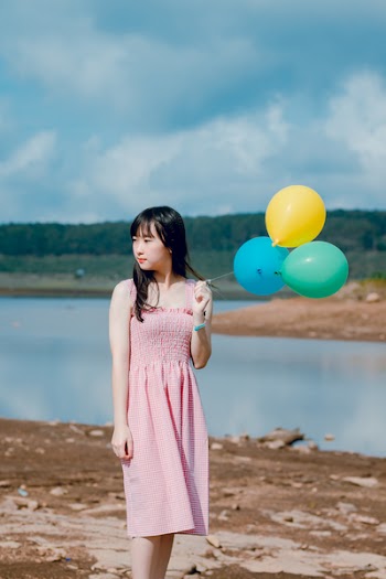 Woman Wearing Pink Dress Holding Three Balloons Near Body of Water