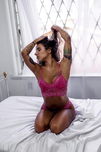Woman Wearing Pink Lingerie Kneeling on Top of Bed While Tying Hair