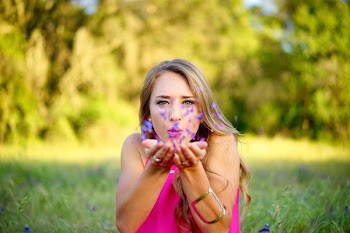 woman wearing pink sleeveless top blowing purple flowers