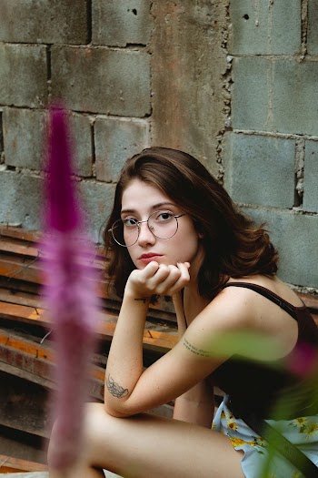 Woman Wearing Purple Tank Top Sitting Near Gray Concrete Wall