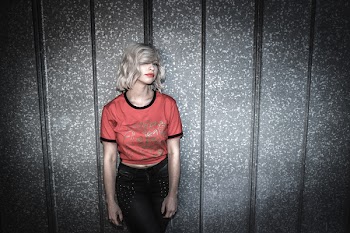 Woman Wearing Red and Black Scoop-neck Shirt and Black Bottoms Leaning on Gray Wall