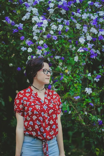 Woman Wearing Red and Blue Shirt Standing Beside Purple and White Flowers
