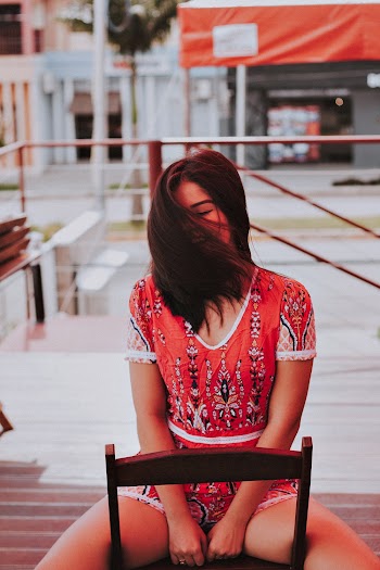 Woman Wearing Red Blouse and Short Sitting on Brown Wooden Chair