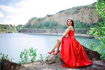 Woman Wearing Red Gown Sitting on Rock Near Body of Water