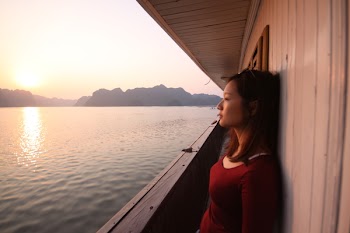 Woman Wearing Red Long-sleeved Scoop-neck Top Leaning on White Wall by the Sea during Golden Hour