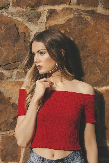 Woman wearing red off-shoulder crop top leaning on a wall