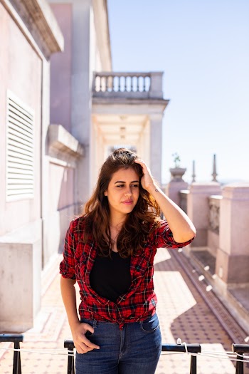 Woman wearing red plaid shirt touching her hair leaning on metal rail