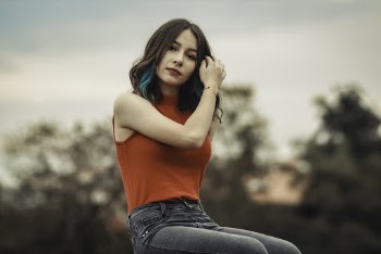 Woman Wearing Red Sleeveless Blouse Sitting While Touching Her Hair