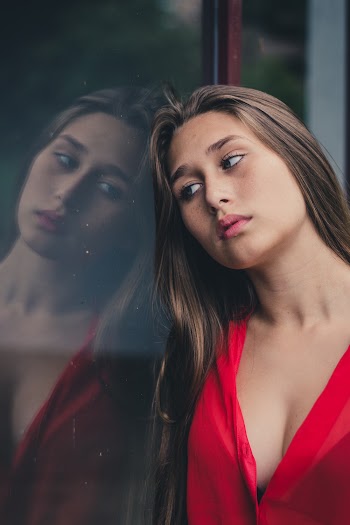Woman Wearing Red V-neck Top Leaning on Glass Wall