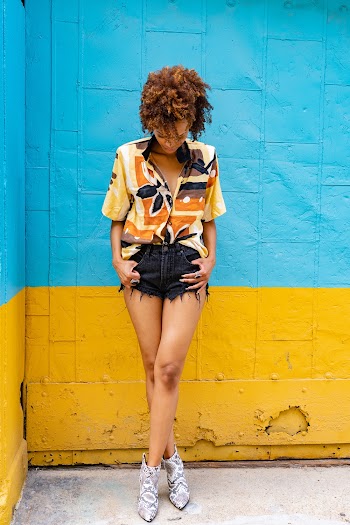Woman Wearing Short Sleeved Shirt and Shorts Posing Near Yellow and Teal Wall