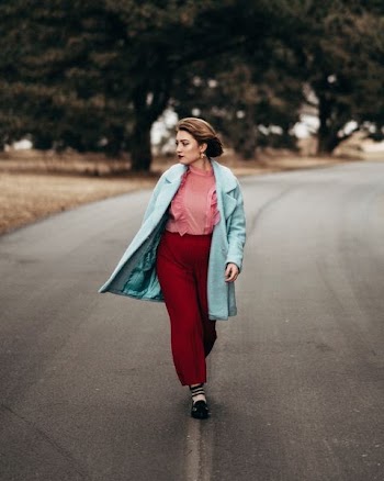 woman wearing teal coat and red pants walking on gray top road at day time