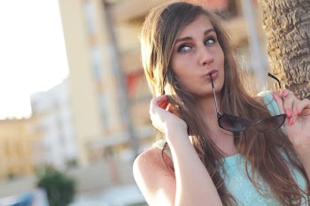 Woman Wearing Teal Floral Tank Top Holding Black Framed Sunglasses Near Tree Posing for a Picture during Daytime