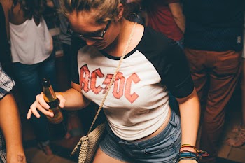 Woman Wearing White and Black Shirt With Acdc Print Holding Brown Glass Bottle