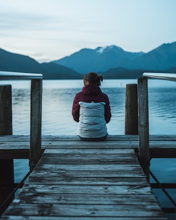 Woman Wearing White and Marron Jacket Sitting on Brown Wooedn Boardwalk