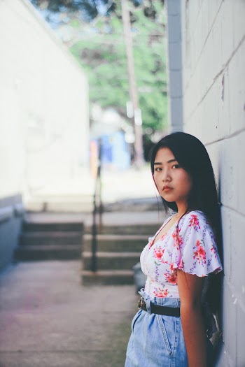 Woman Wearing White and Orange Floral Blouse Leaning Against White Wall While Glancing Her Left Side