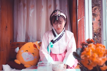 Woman Wearing White and Pink Traditional Korean Dress Sitting Near Yellow Plush Toy