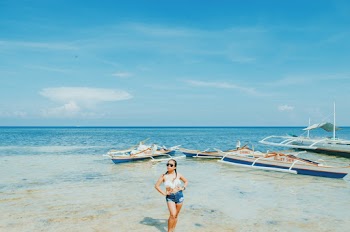 Woman Wearing White Bikini Top and Blue Short Shorts Standing Withe Both Arms Akimbo Near Sea Under Blue and White Sky