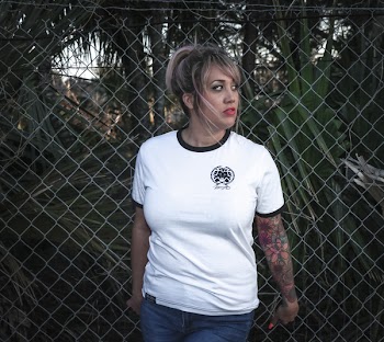 Woman Wearing White Crew-neck T-shirt With Black Trim and Blue Denim Bottoms Beside Wire Fence