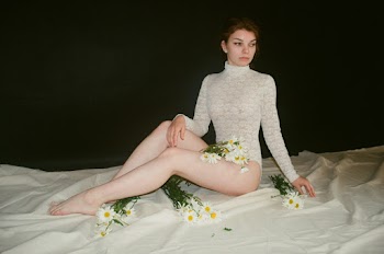 Woman Wearing White Crochet Leotard Sitting on Brown Carpet With Flowers