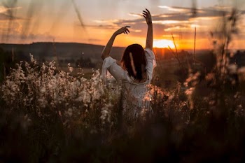 woman wearing white dress raising her two hands surrounded white petaled flowers during sunset