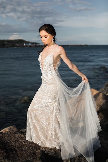 Woman Wearing White Floral Wedding Dress Standing On Rocks Near Body Of Water