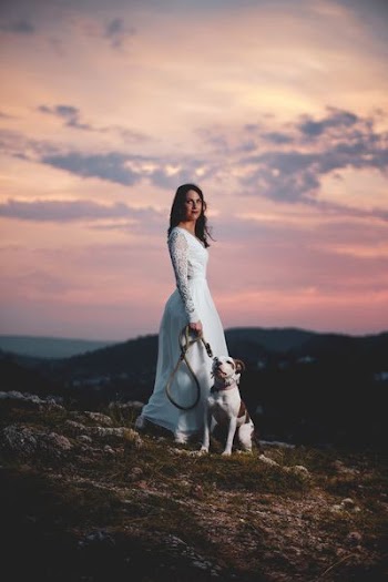 woman wearing white lace gown with dog sitting on the ground
