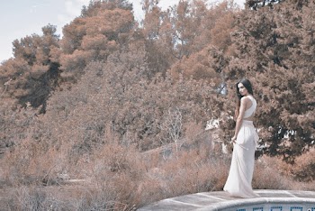 Woman Wearing White Long-Dress Standing On The Side Of  A Pool Surrounded By Trees And Shrubs