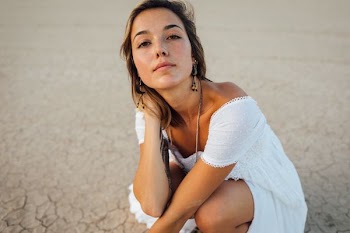 woman wearing white off-shoulder dress sitting on sand